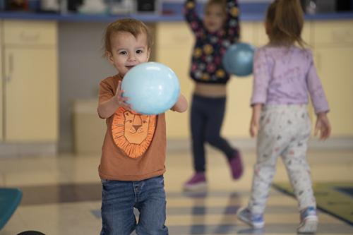 A toddler happily plays with a ball in the playroom