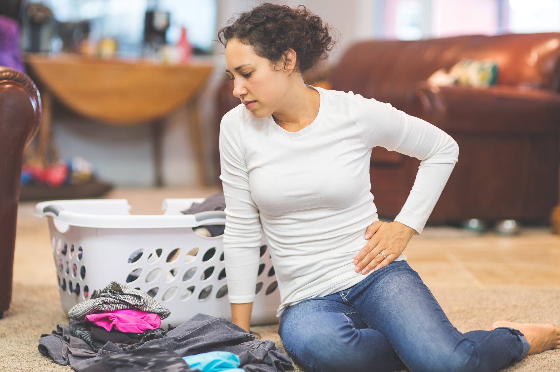 Woman experiencing pelvic pain while folding laundry on the floor
